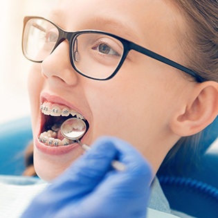 A young girl wearing glasses allowing her orthodontist in Bethel Park to perform a checkup of her braces