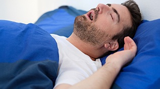 A middle-aged man asleep in bed with his mouth open and snoring