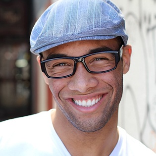 A young male wearing a hat and glasses smiles after completing his treatment with braces in Bethel Park