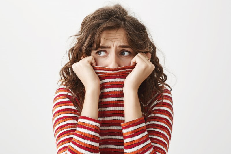 Scared woman covering her smile with her sweater